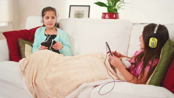 Two Girls Lie On A Couch Together And Sing Along To The Music On