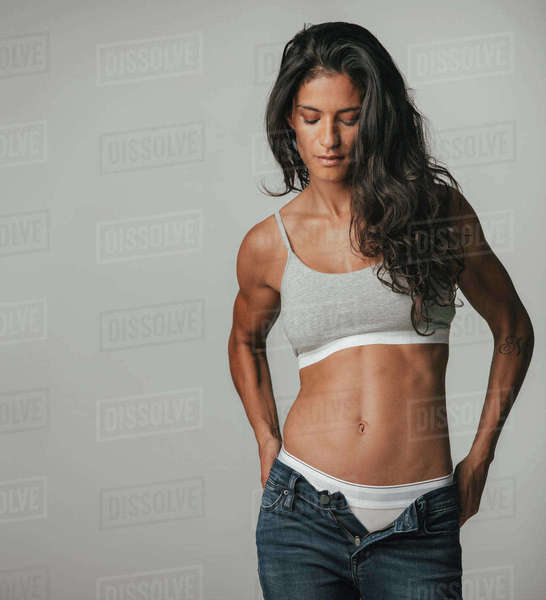 Fit young woman pulling down pants with copy space to her side over