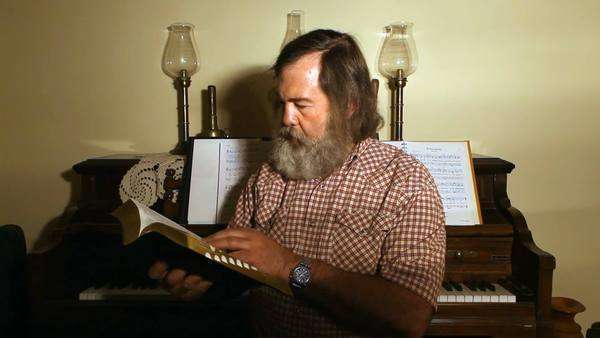 Mature Man Sitting By A Piano Reading The Bible Long Hair And