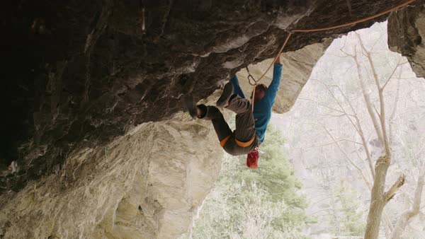 Man Hanging And Rock Climbing On Ceiling Of Cave Opening Stock