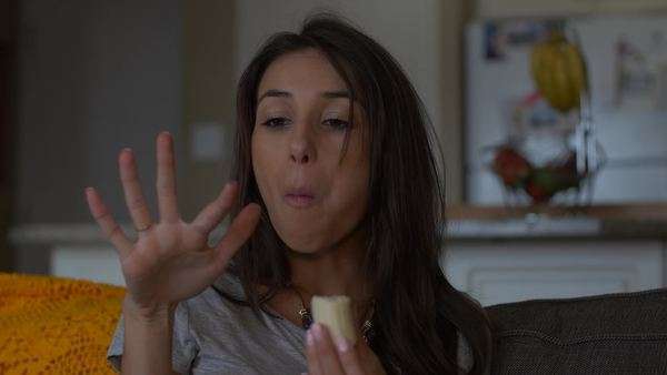 Attractive Woman On Couch Eats Piece Of Banana From Hand While