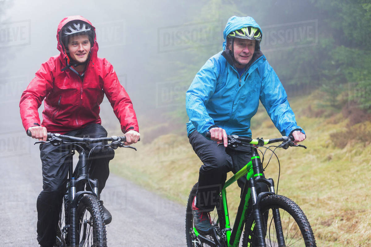 Father and son mountain biking in rain Stock Photo Dissolve