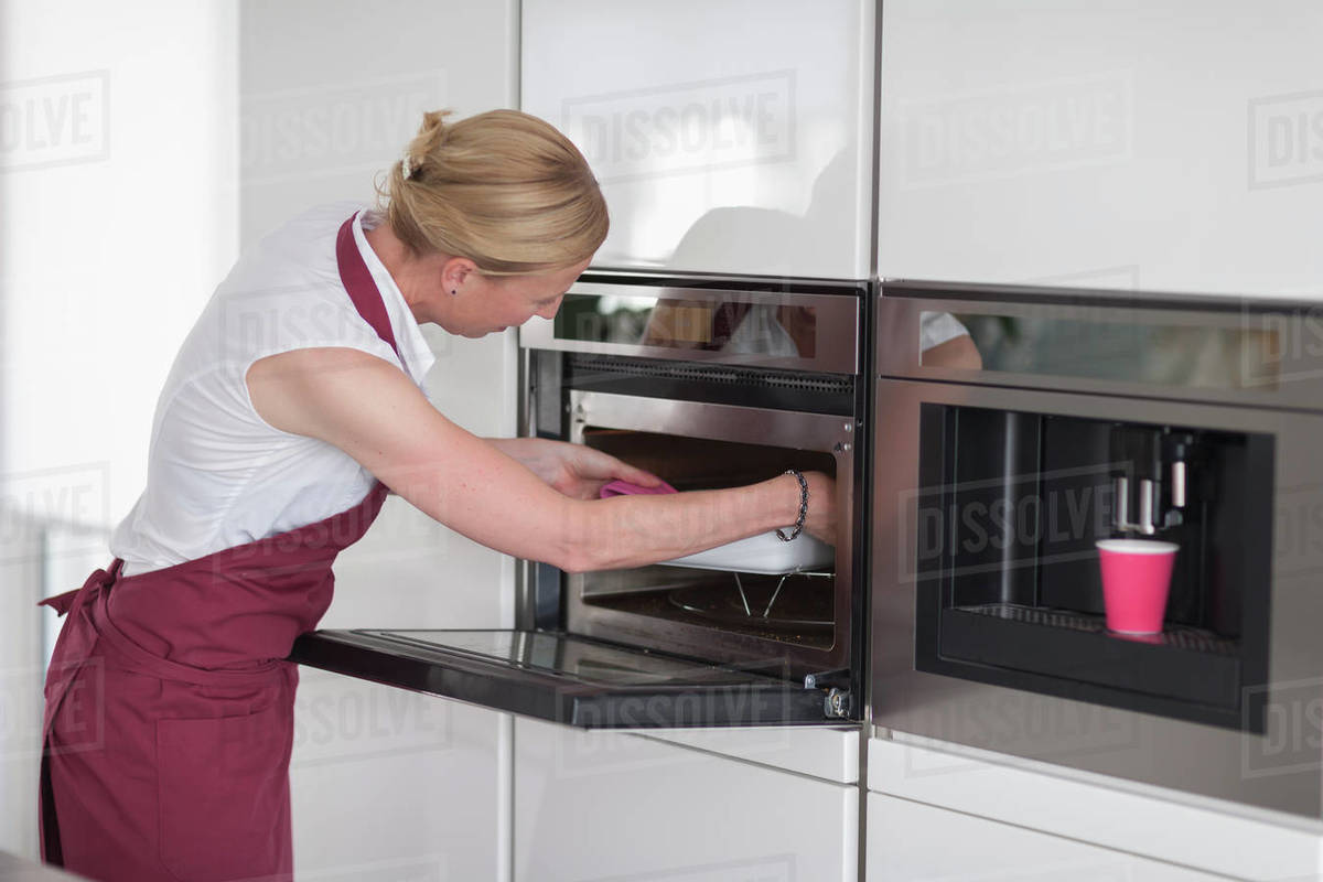 Woman using oven in kitchen Stock Photo Dissolve