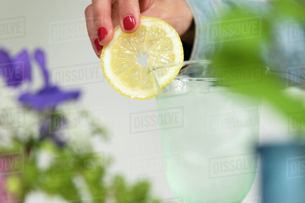 Woman putting lemon slice on glass of water Stock Photo Dissolve