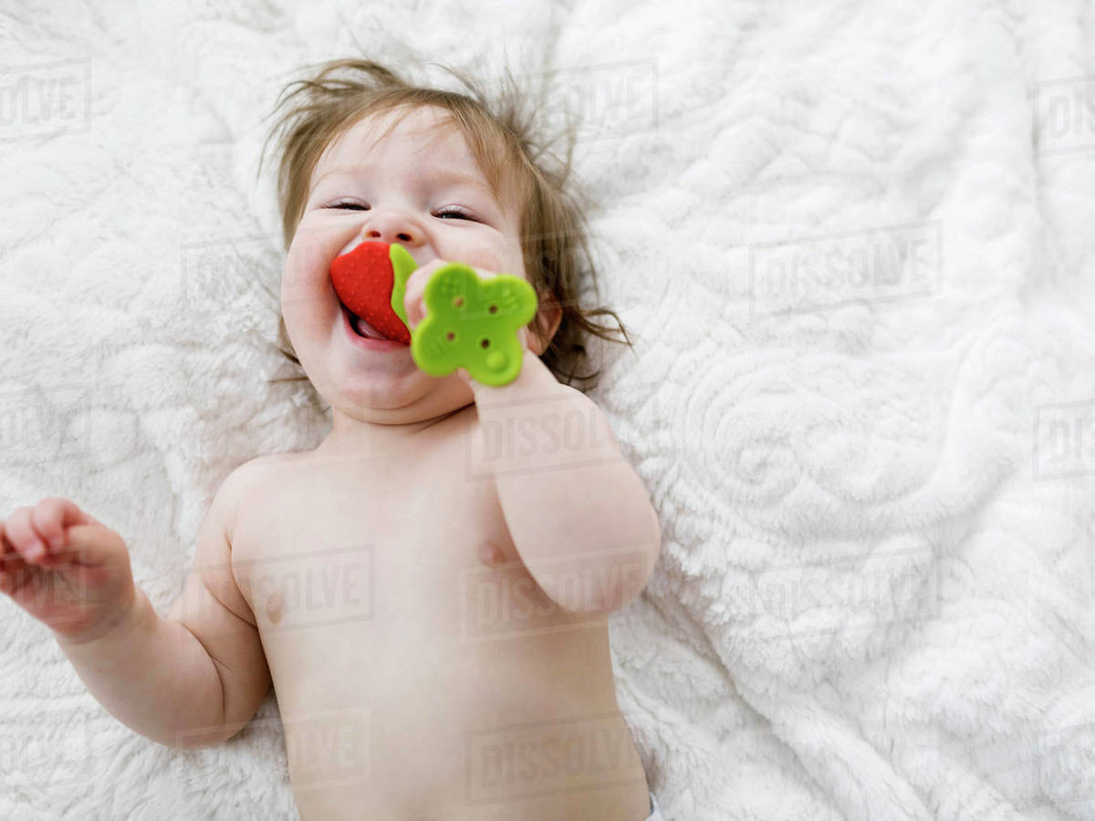 Baby girl lying on blanket biting strawberry toy Stock Photo Dissolve
