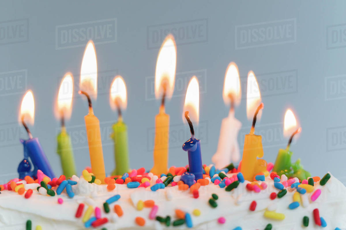 Lit birthday candles on cake Stock Photo Dissolve