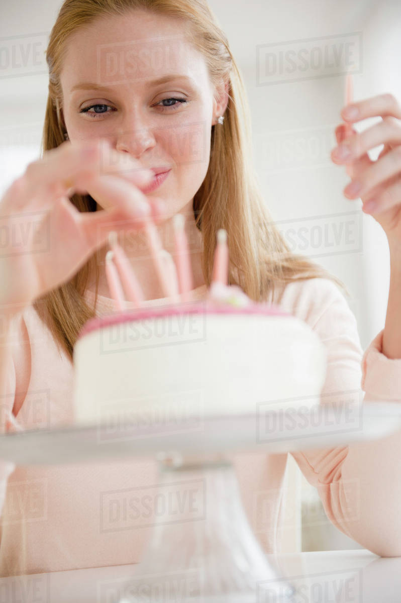 Woman putting candles on birthday cake Stock Photo Dissolve