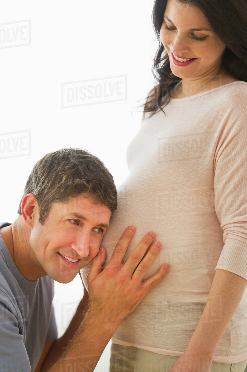 Man putting ear to pregnant woman's belly Stock Photo Dissolve