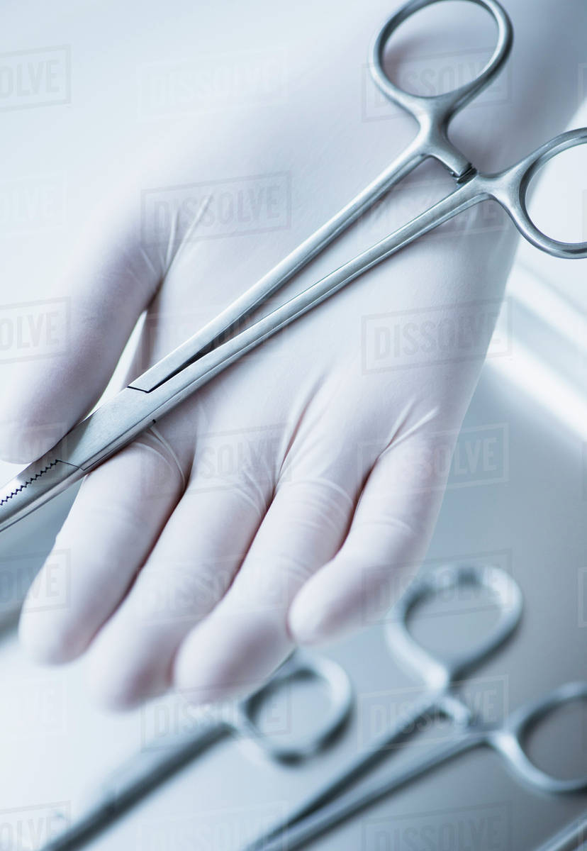 Close up of hand in surgical glove holding dental forceps, studio shot