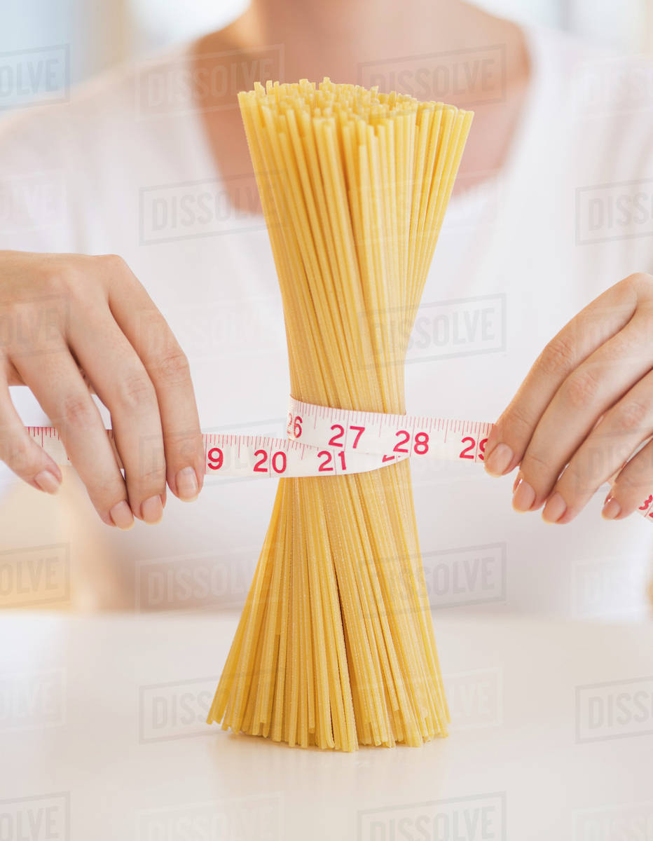 Close up of woman's hands measuring pasta with tape measure Stock