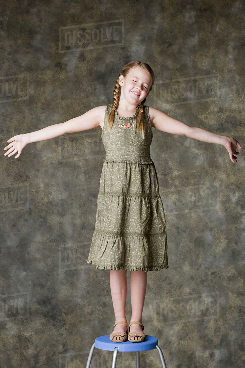 Portrait of smiling girl (89) standing on stool, studio shot Stock Photo Dissolve