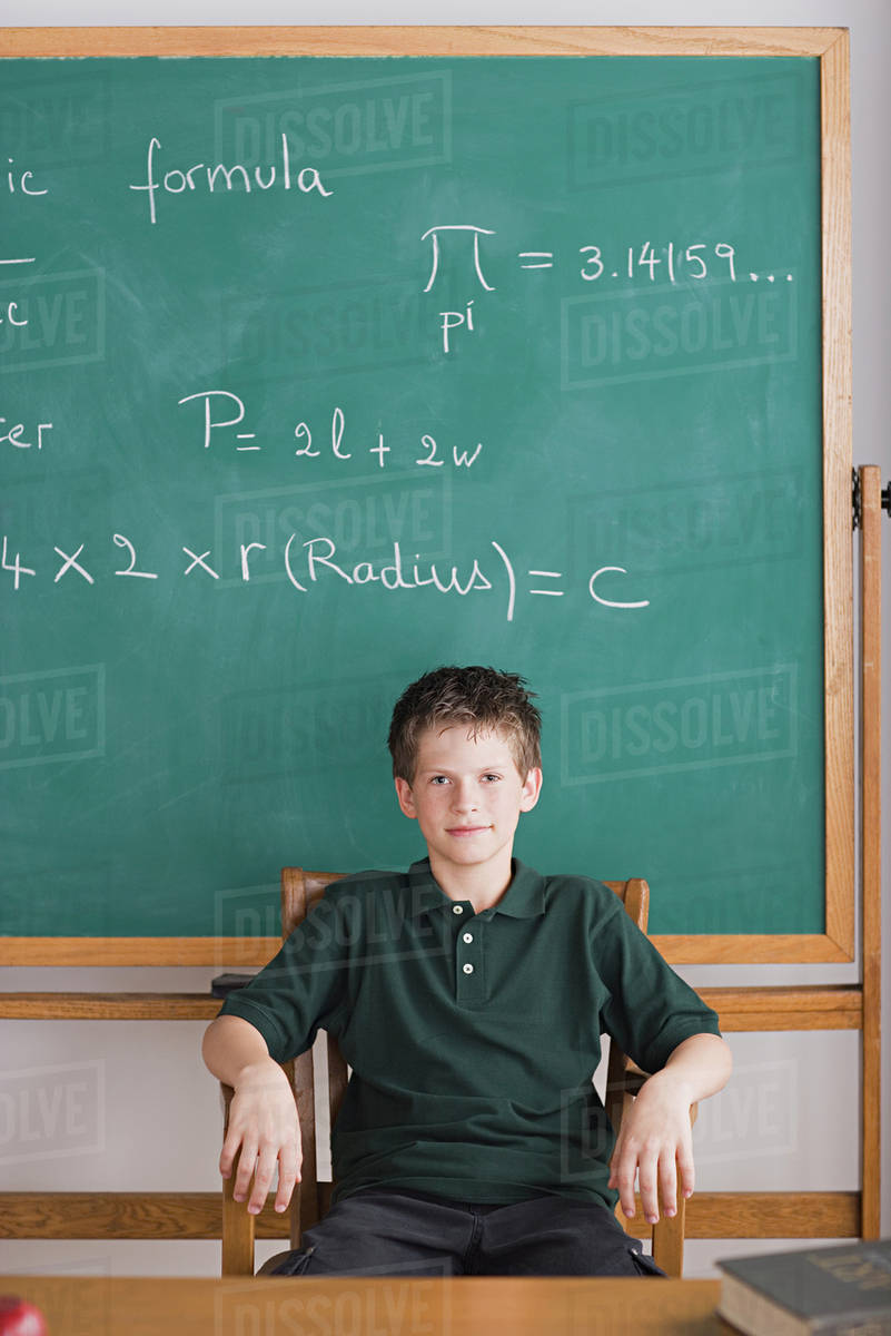 Boy sitting in teachers chair, blackboard in background Royalty