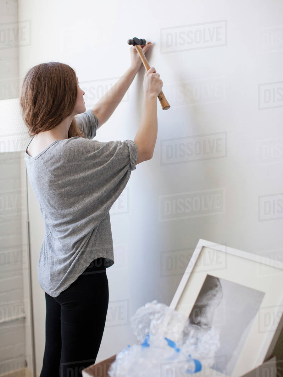 Young woman hanging picture on freshly painted wall Stock Photo