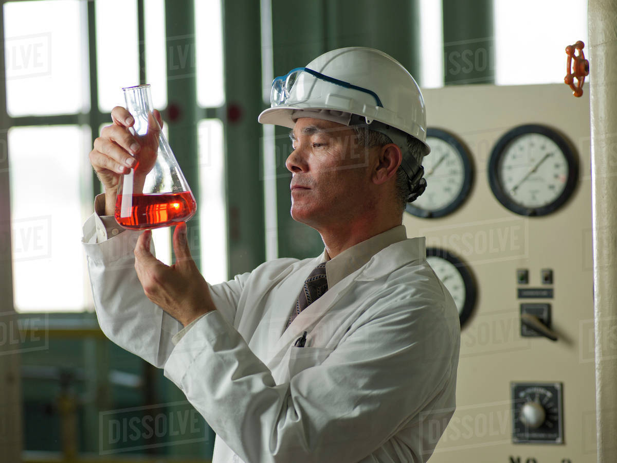Worker in lab coat examining liquid in beaker Stock Photo Dissolve