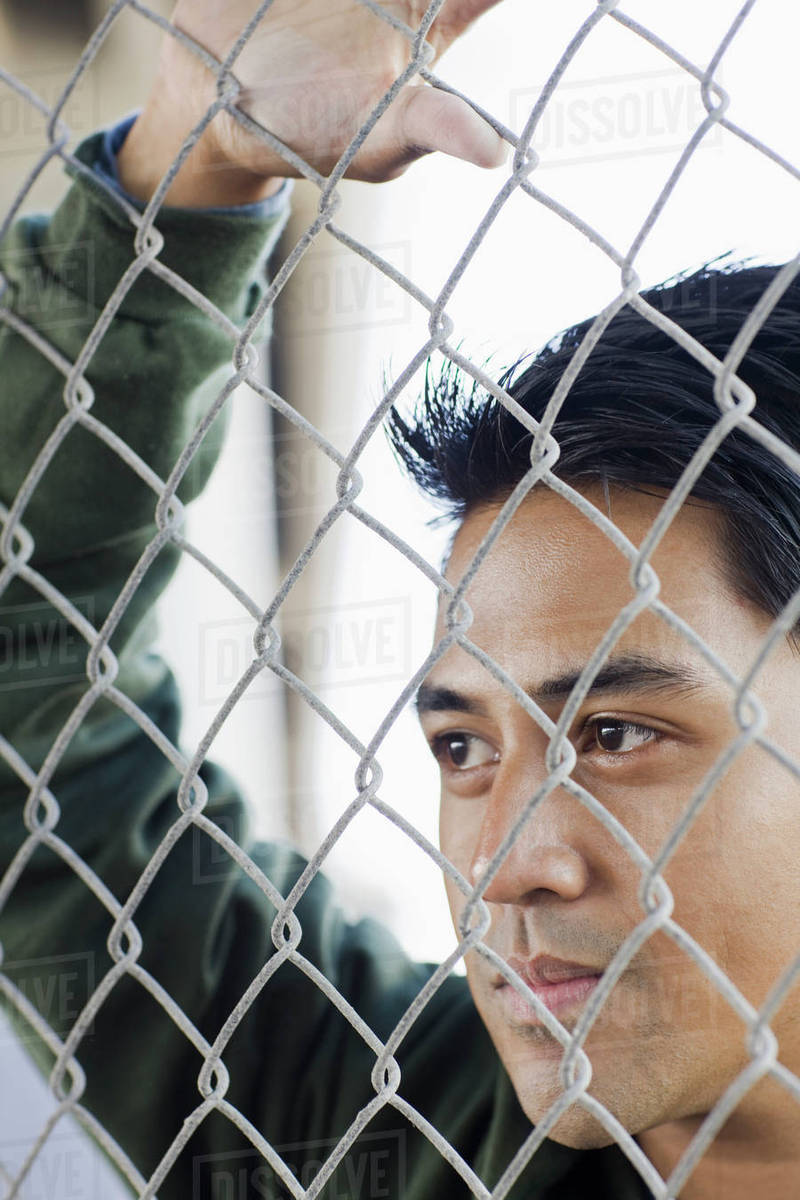 Close up of young man leaning against chain-link fence - Royalty-free Stock  Photo | Dissolve
