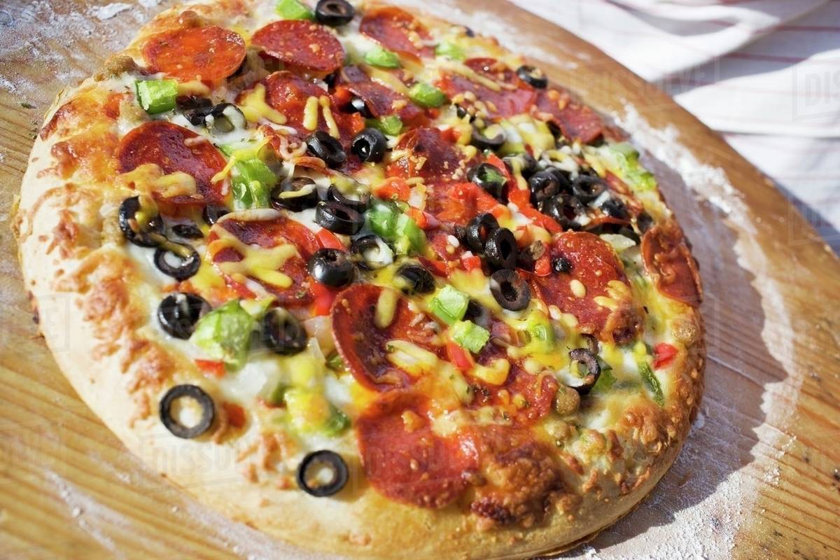 Pepperoni pizza with peppers and olives on wooden plate Stock Photo