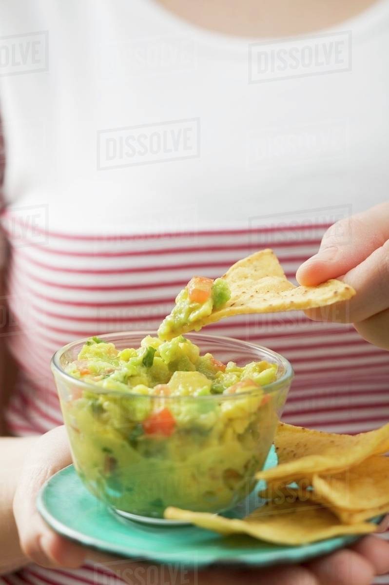 Woman dipping tortilla chip in guacamole Stock Photo Dissolve
