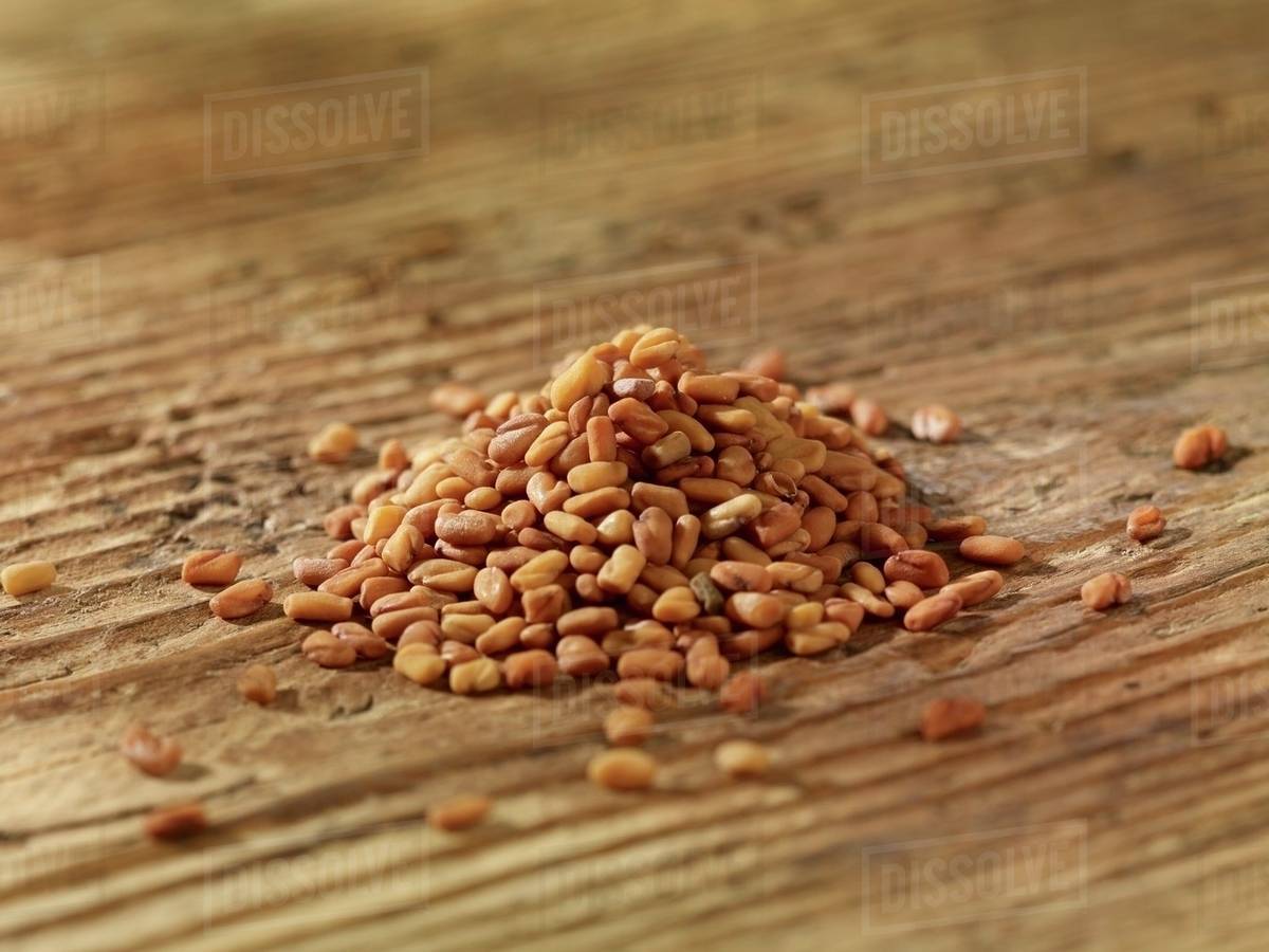 A pile of fenugreek seeds on a wooden surface Stock Photo Dissolve