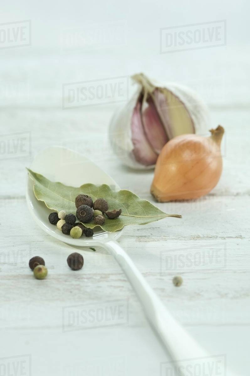 A bay leaf, pepper corns and allspice berries on a spoon with an onion