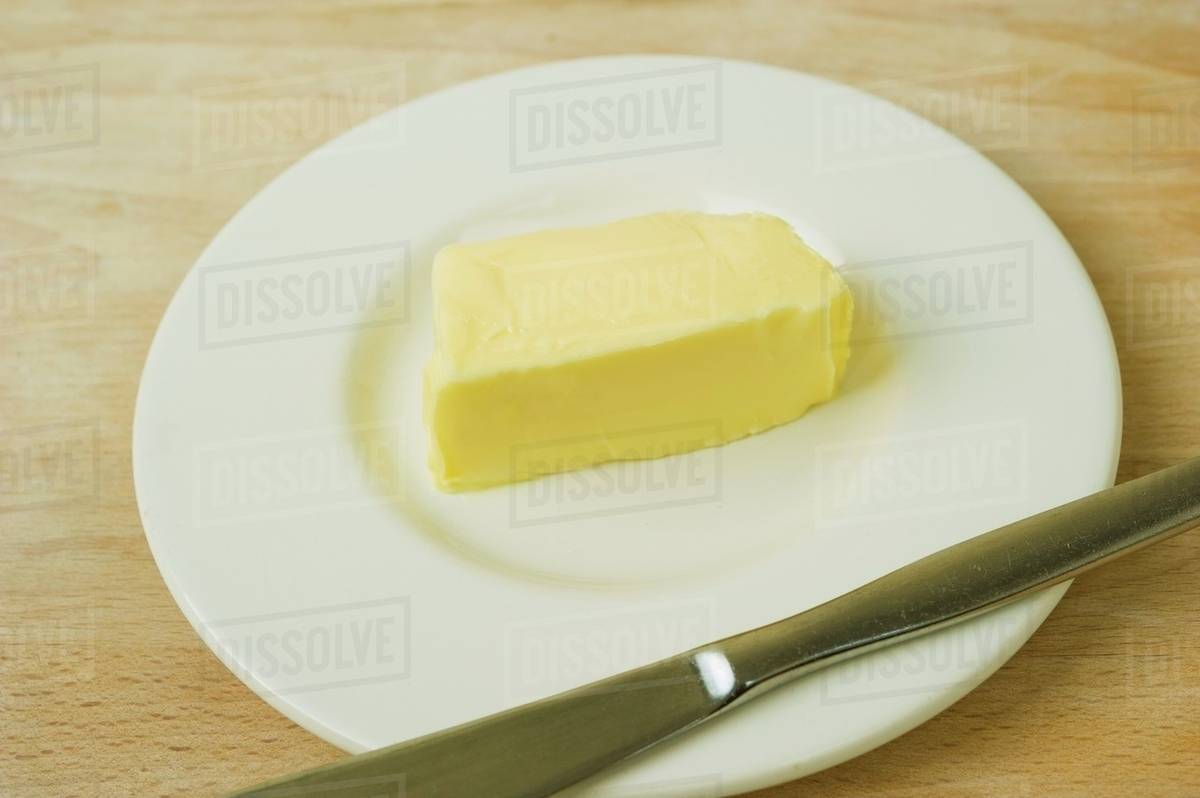 A pat of butter on a plate with a knife Stock Photo Dissolve