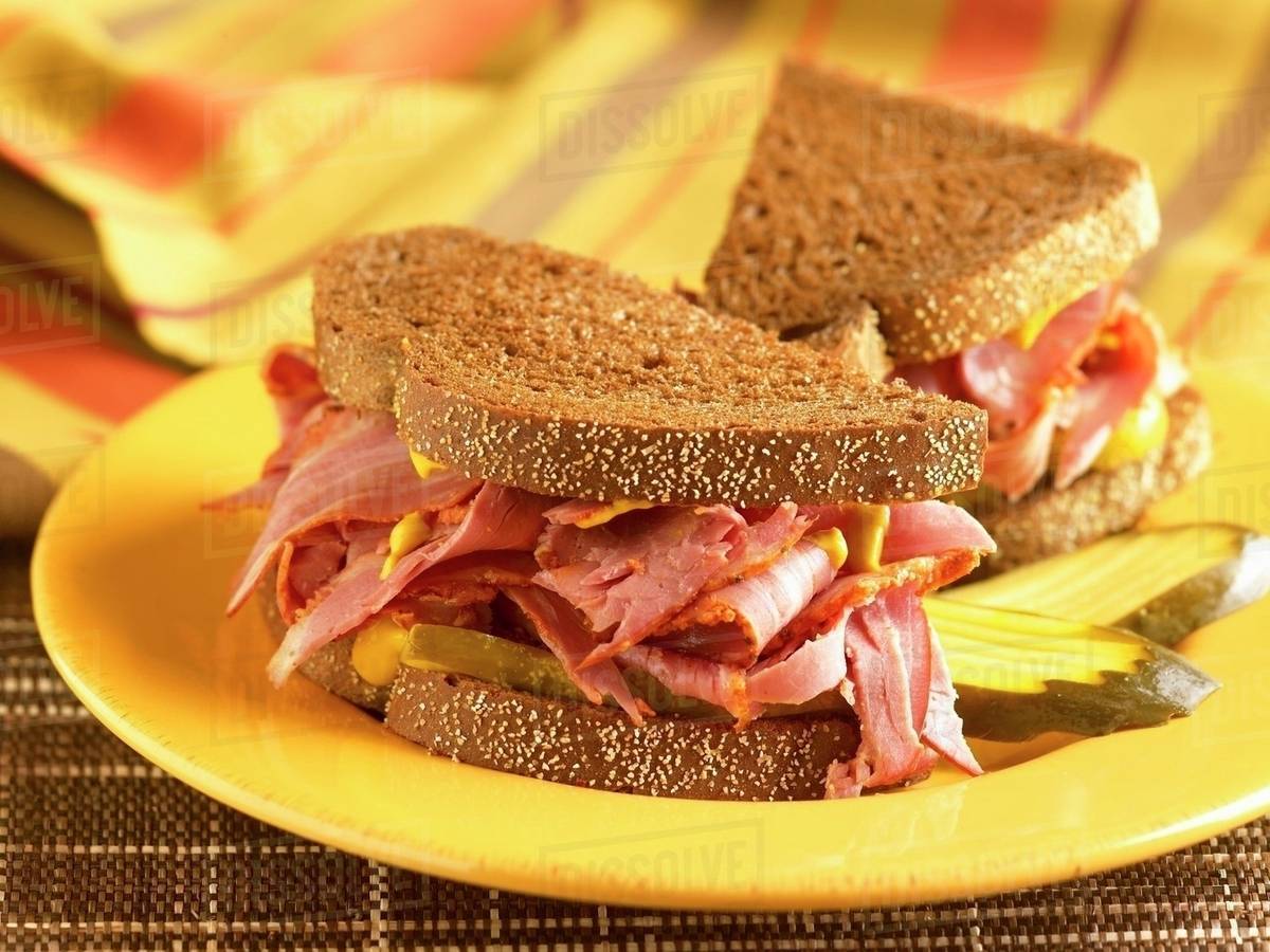 Corned Beef Sandwich with Mustard and Pickles on Pumpernickel Bread; Halved on a Yellow Plate