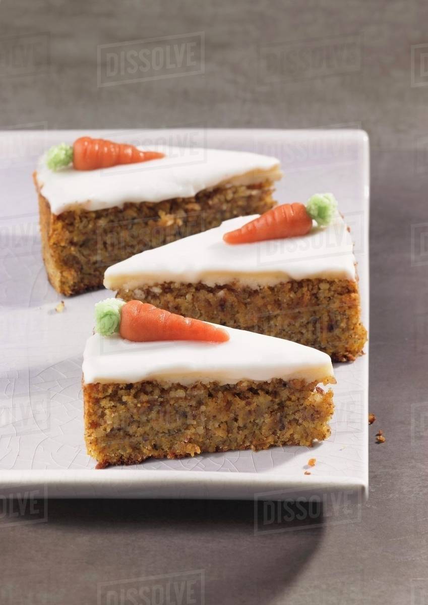 three slices of carrot cake topped with icing and marzipan carrots