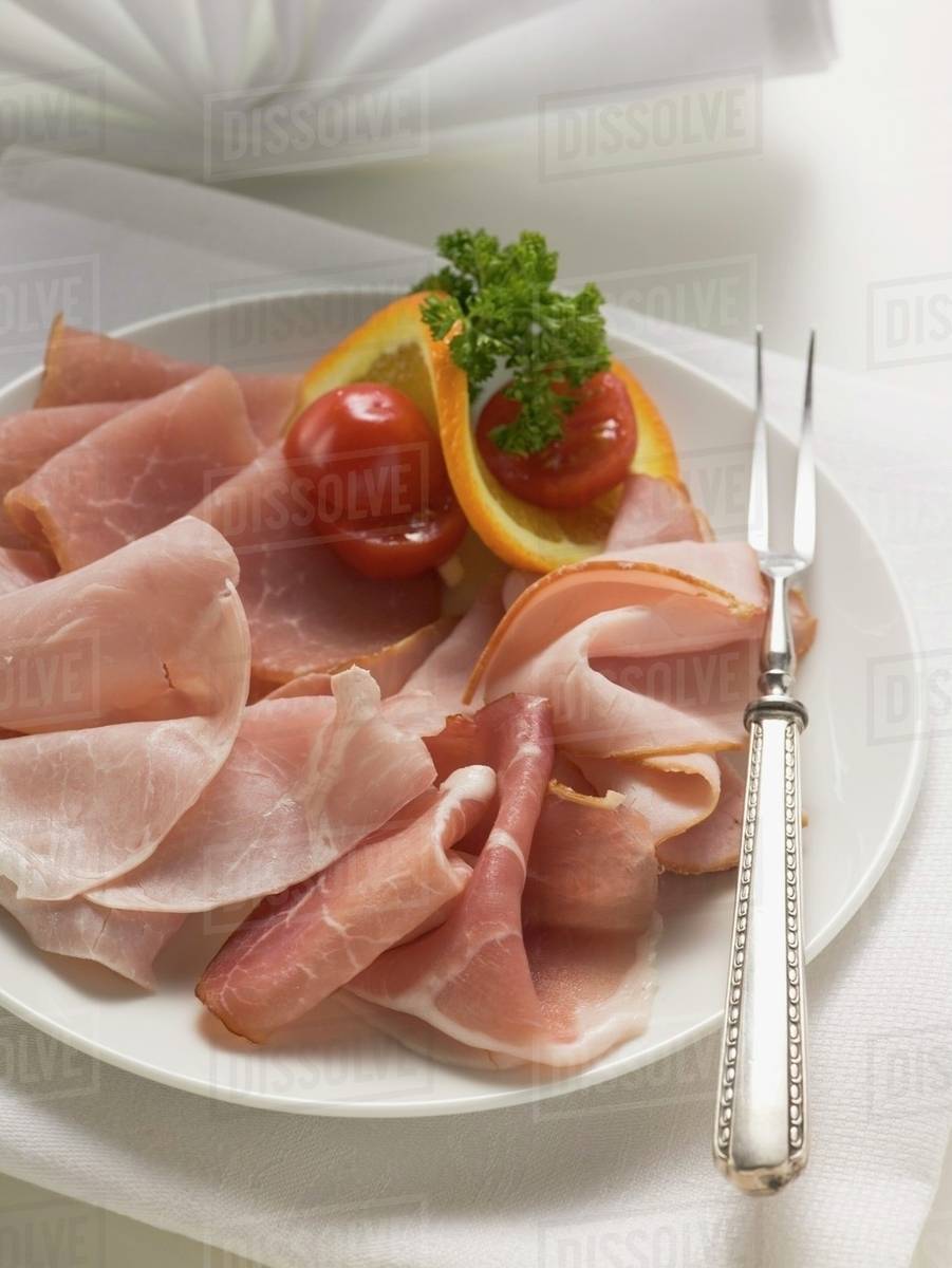 Various types of ham on a plate with meat fork Stock Photo Dissolve