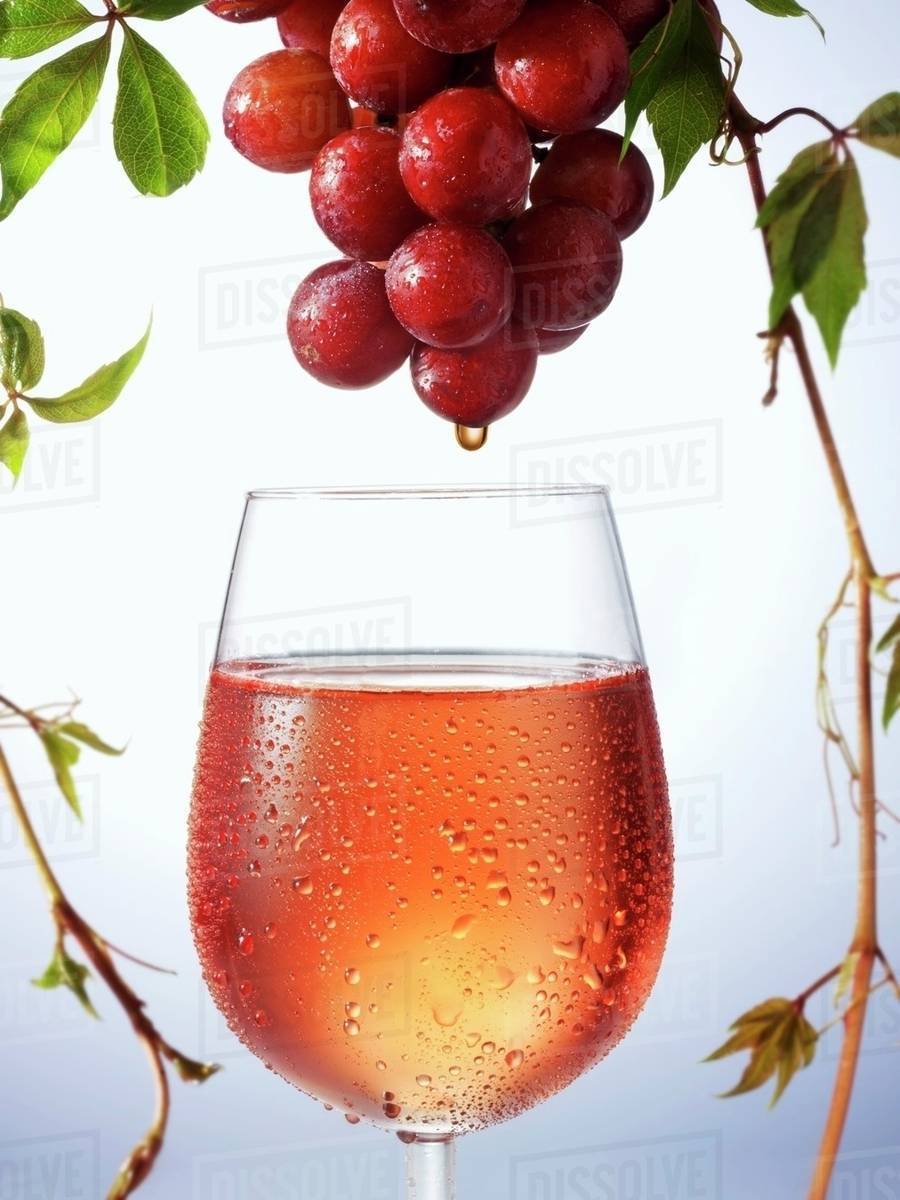 Rose wine dripping from grapes into wine glass Stock Photo Dissolve