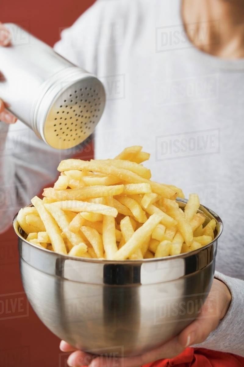 Putting salt on chips in a bowl Stock Photo Dissolve