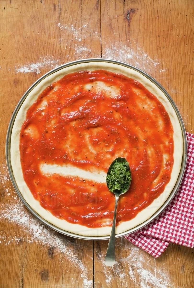 Pizza base with tomato sauce and spoonful of oregano Stock Photo