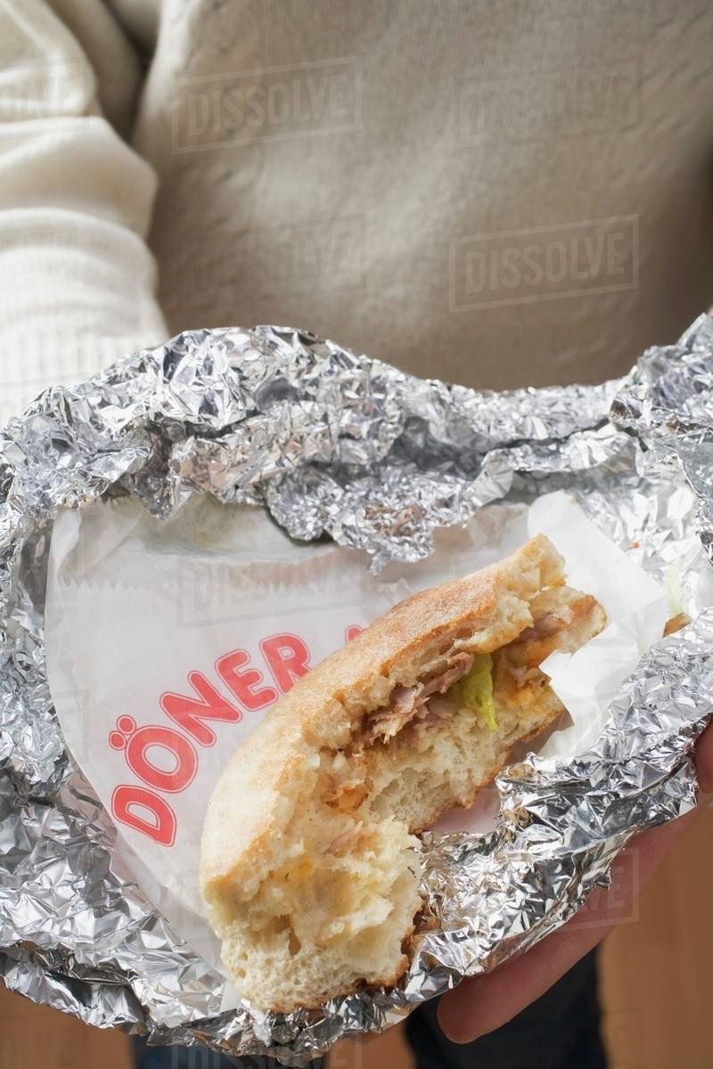 Person holding doner kebab, partly eaten, in aluminium foil Stock