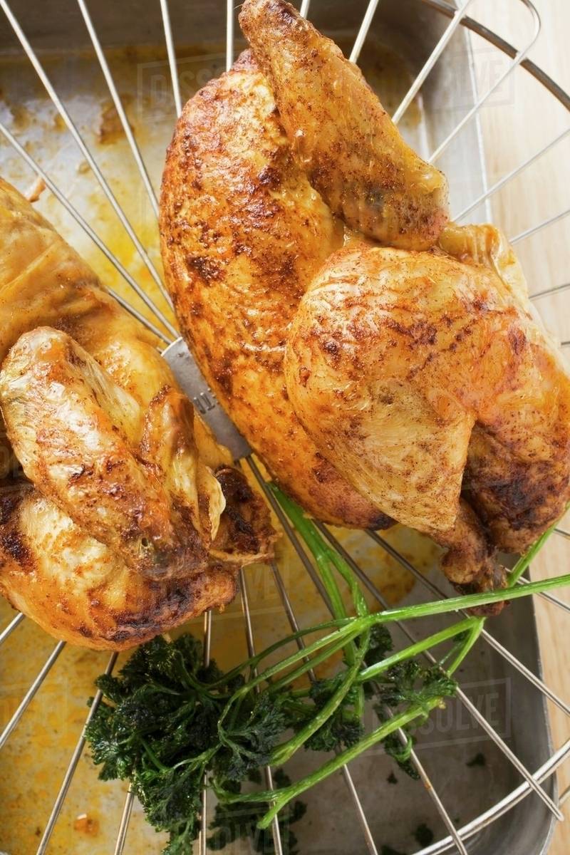 Two half roast chickens on rack above roasting tin Stock Photo Dissolve