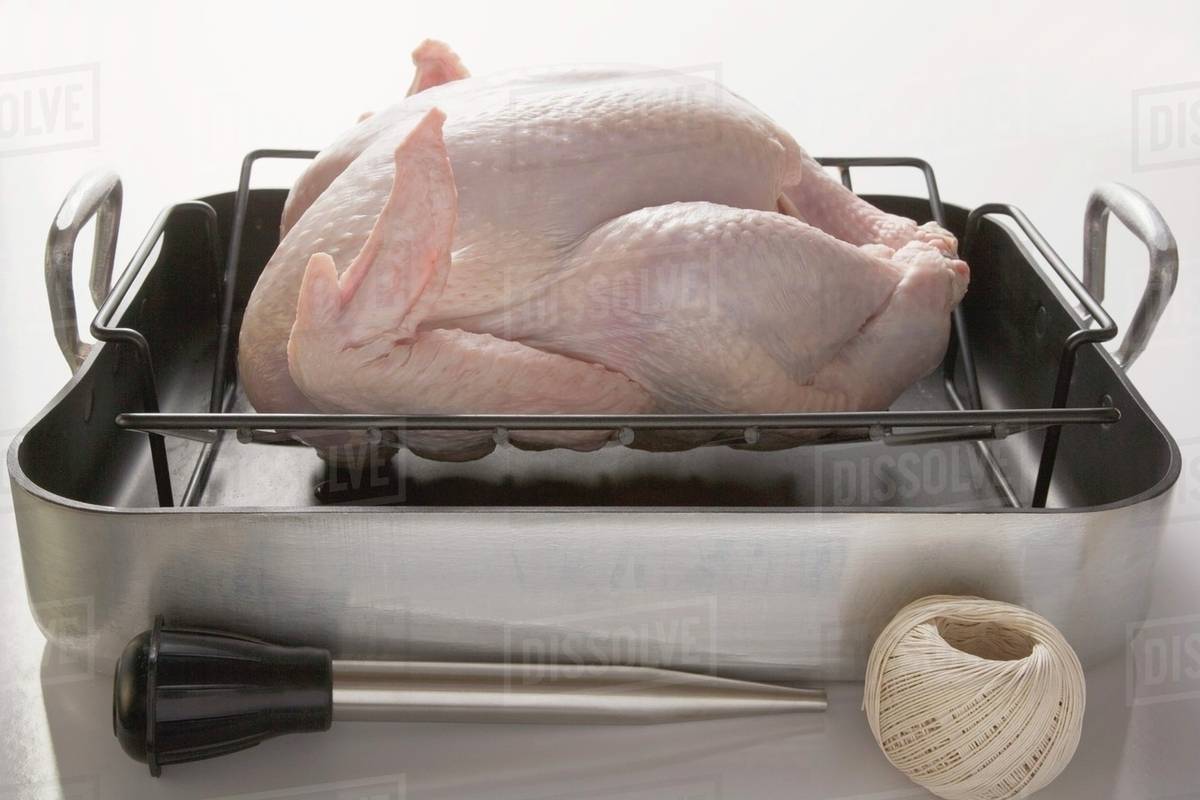 Chicken in roasting tin, kitchen utensils beside it Stock Photo