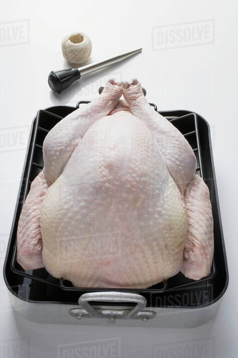 Whole raw turkey in roasting tin, baster, kitchen string Stock Photo Dissolve