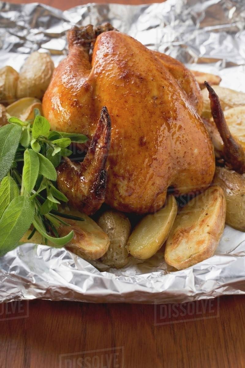 Roast chicken with potatoes and herbs on aluminium foil Stock Photo
