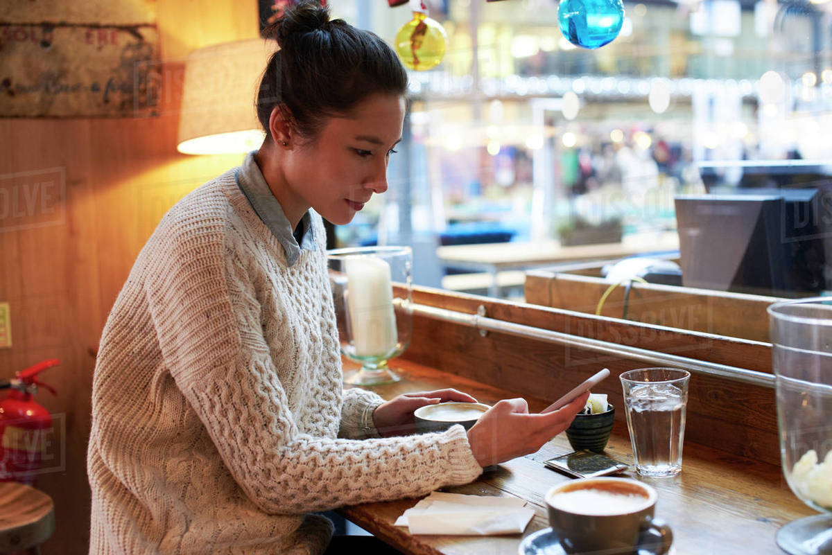 Young woman sitting in coffee shop reading text message - Royalty-free ...