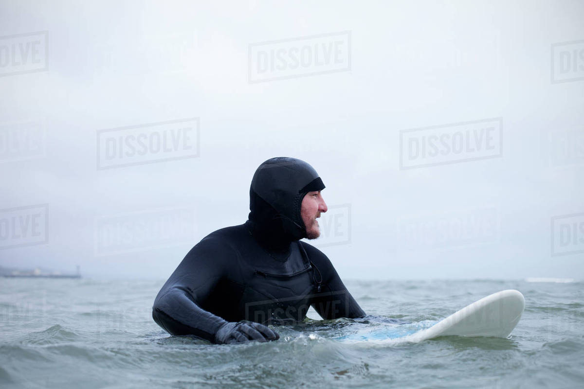 Surfer wearing wetsuit floating with board in wintery sea Stock Photo