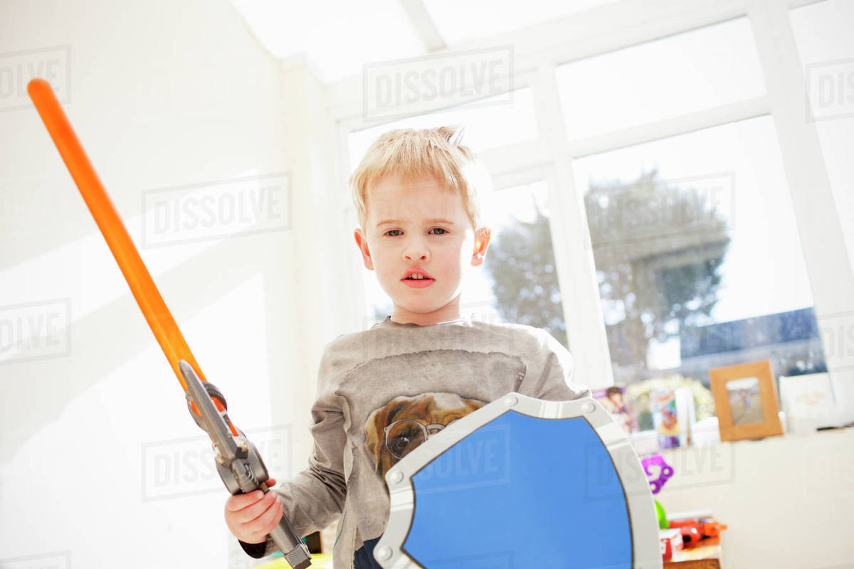 Boy playing with plastic sword and shield at home Stock Photo Dissolve