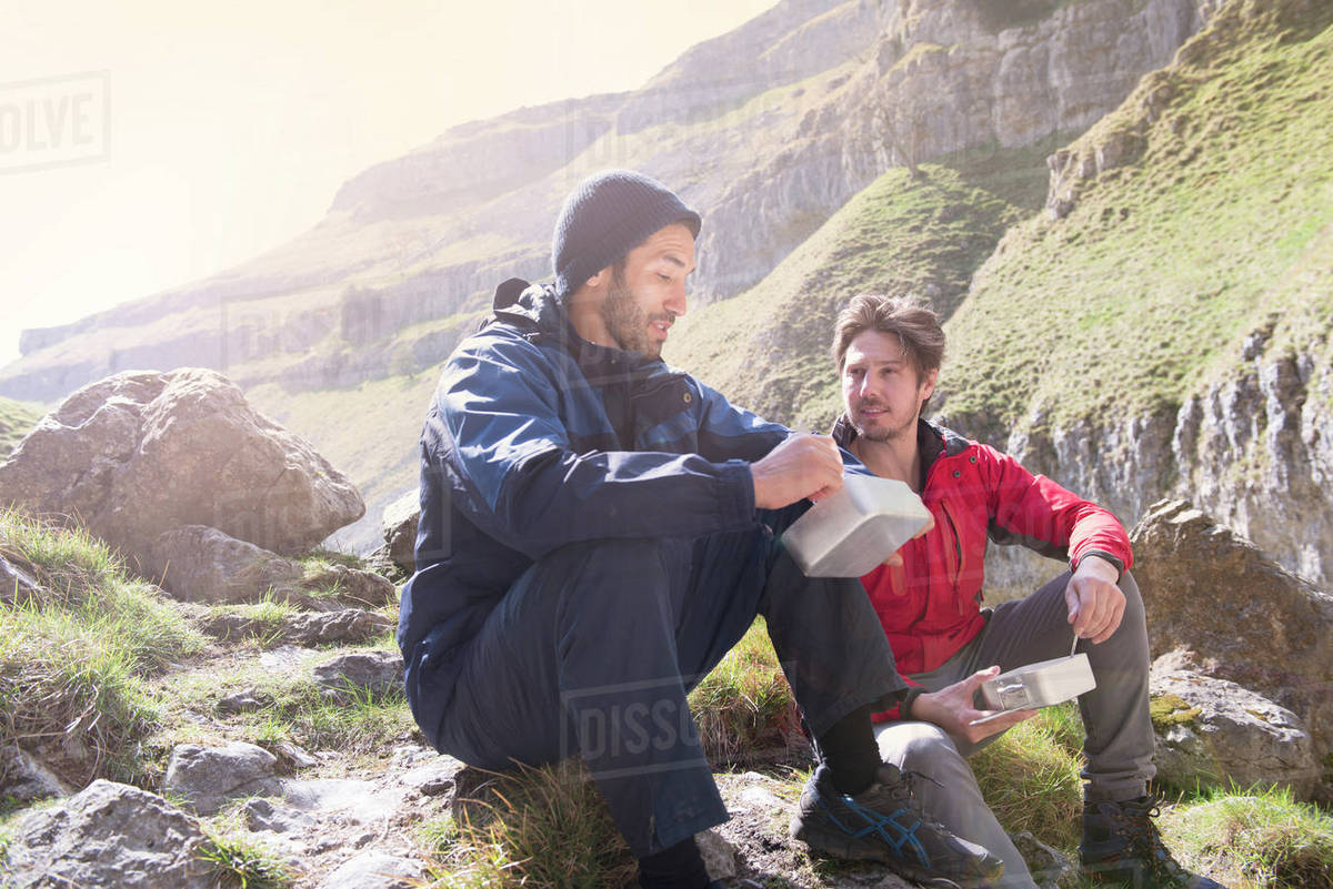 Two mountaineers sitting eating food in rugged terrain Stock Photo
