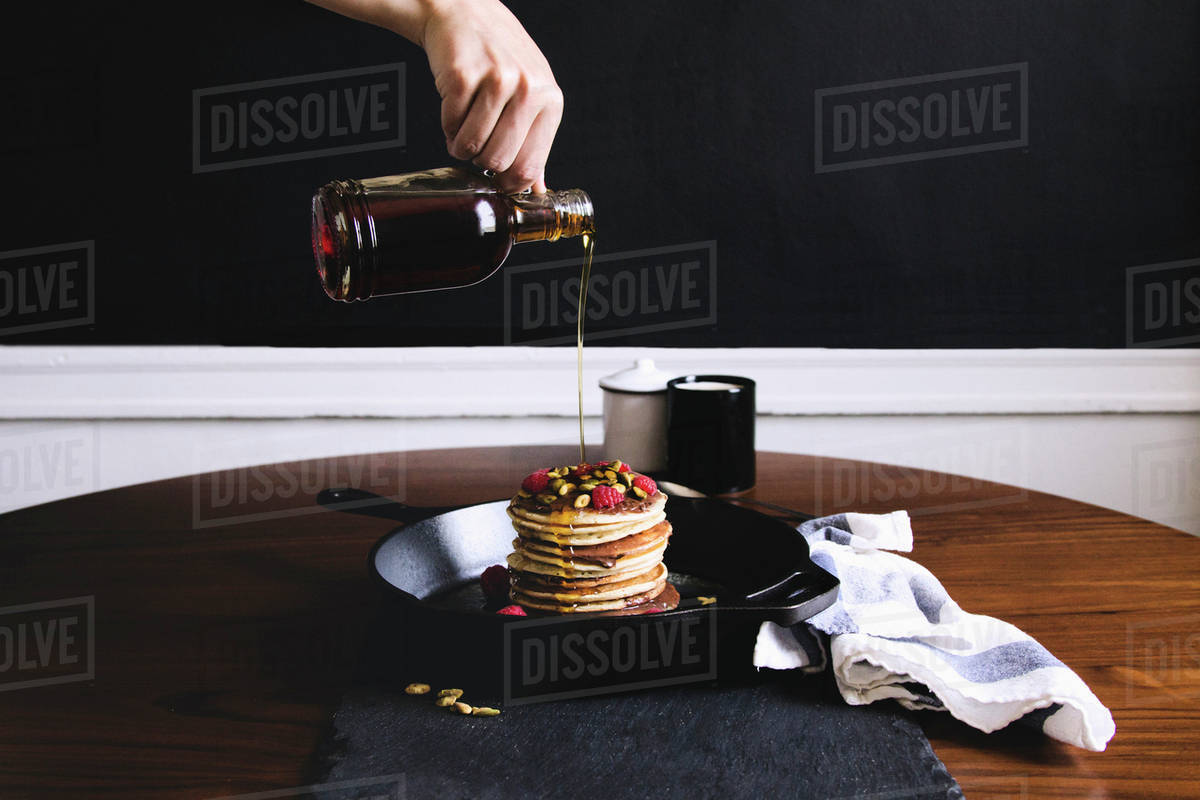 Hand pouring syrup on pancakes Stock Photo Dissolve
