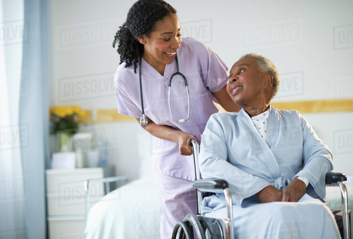 Nurse pushing woman sitting in wheelchair in hospital Stock Photo