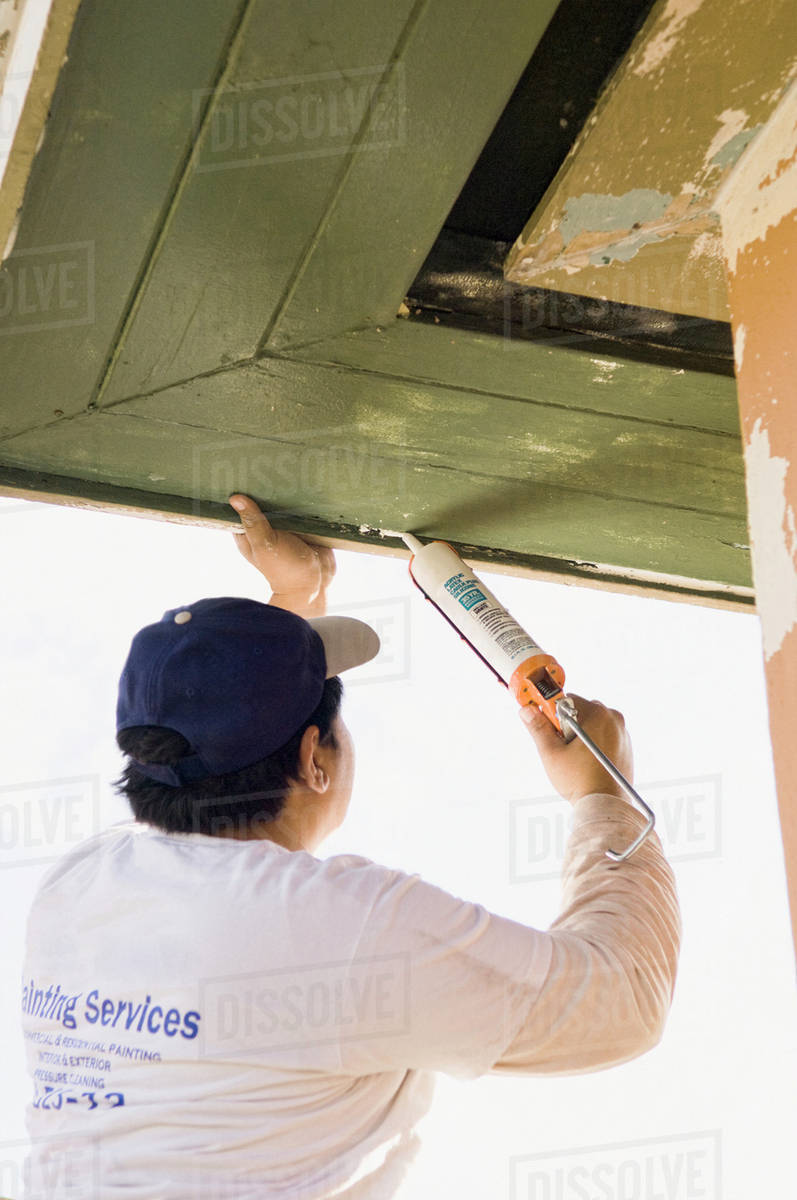 Latin man caulking roof eaves Stock Photo Dissolve