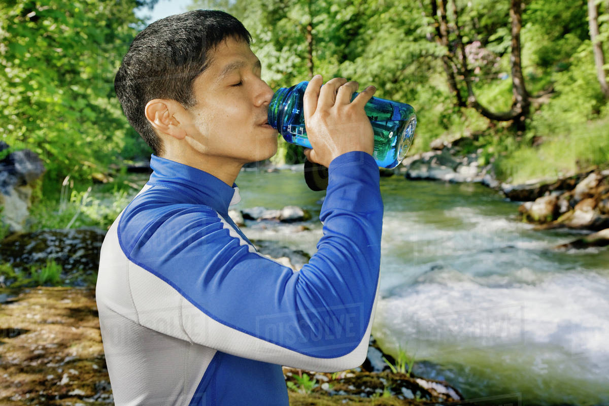 Mixed race man drinking water near river Stock Photo Dissolve