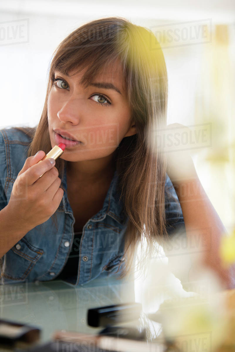 Mixed race woman applying lipstick Stock Photo Dissolve