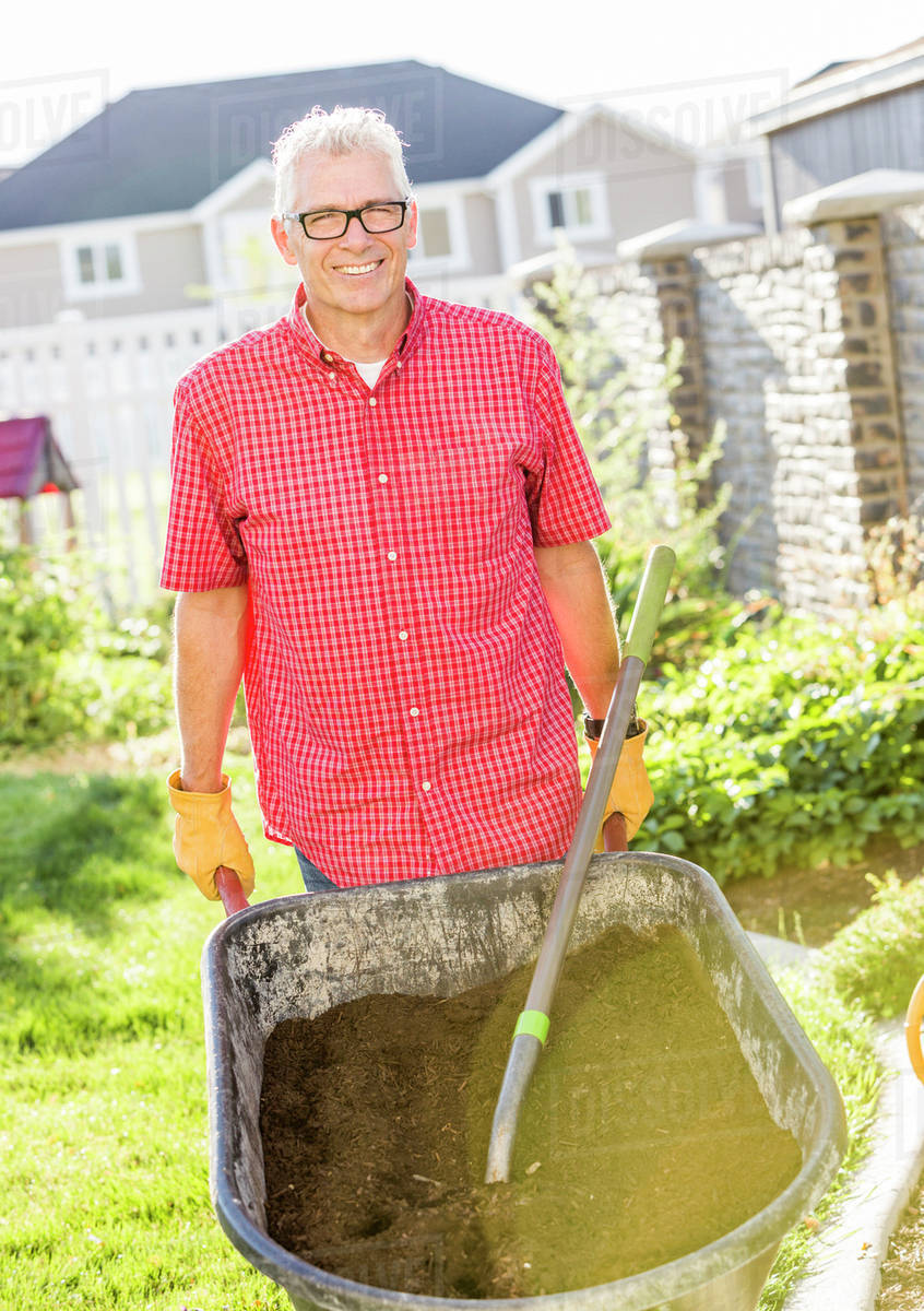 Caucasian man pushing wheelbarrow of dirt Stock Photo Dissolve