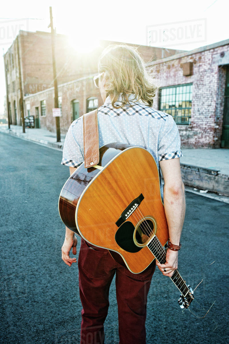 Caucasian man carrying guitar outdoors Stock Photo Dissolve
