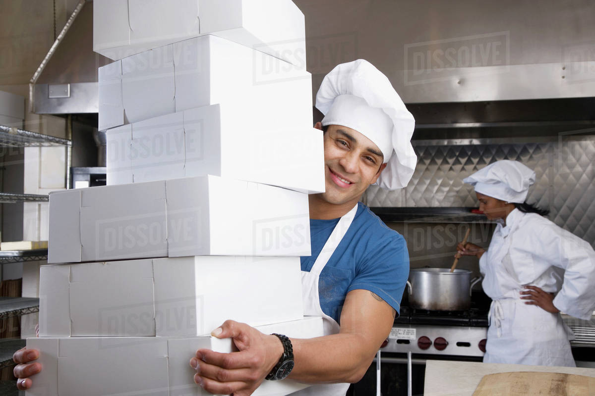Hispanic male pastry chef carrying stack of boxes Stock Photo Dissolve