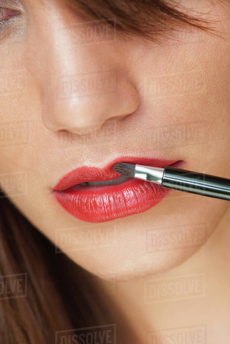 Caucasian woman putting on lipstick with brush Stock Photo Dissolve