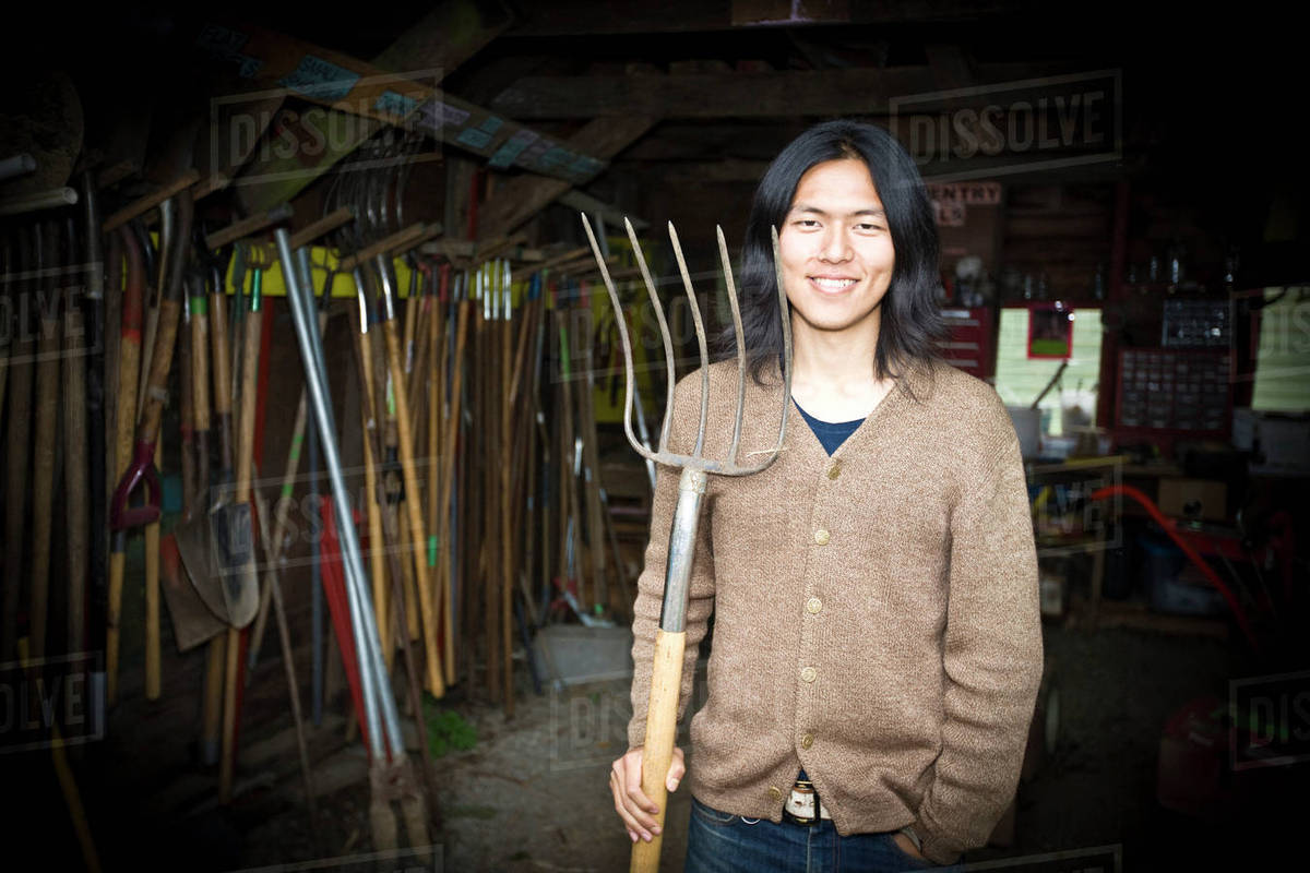 Japanese gardener holding pitchfork in barn Stock Photo Dissolve
