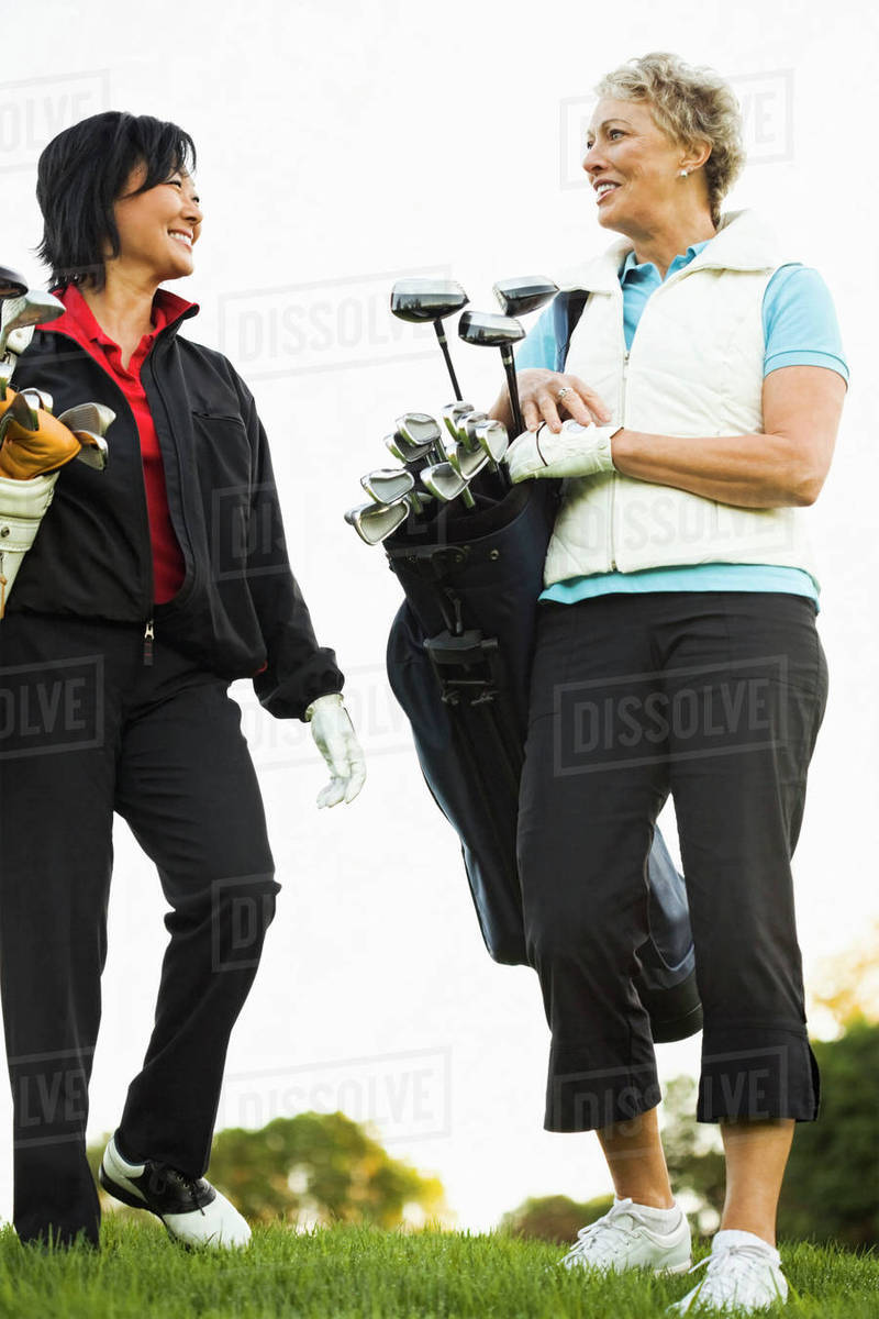 Women carrying golf clubs on golf course Stock Photo Dissolve